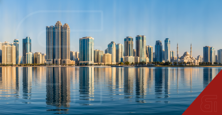 Panoramic view of the Sharjah skyline featuring modern residential skyscrapers and Al Noor Mosque reflecting on calm blue waters under a clear sky.