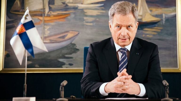 President of Finland seated formally with Finnish flag and microphones, symbolizing official nuclear energy talks with IAEA director.